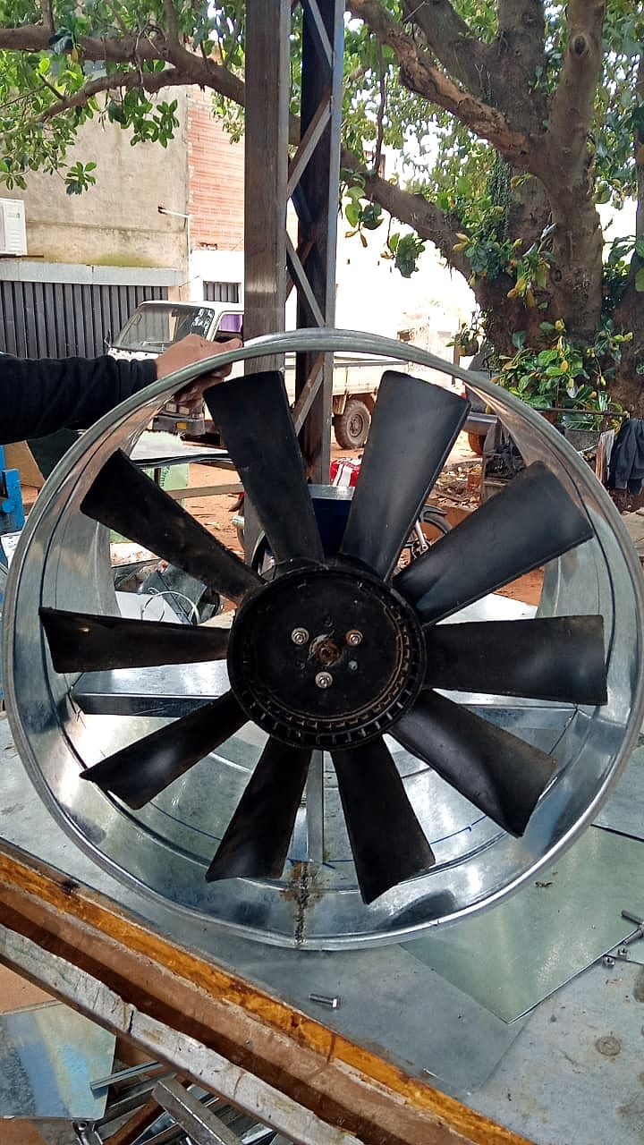 Rotor de aspas negras de un extractor axial dentro de su carcasa cilíndrica de chapa galvanizada, sostenido con una mano en el taller