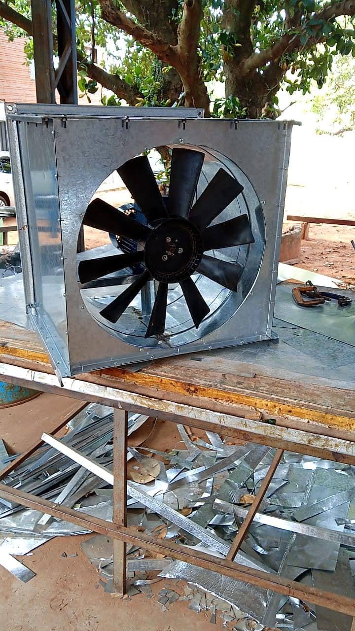 Extractor axial montado en una caja cuadrada de chapa galvanizada, sobre un banco de trabajo, con recortes de chapa en el piso