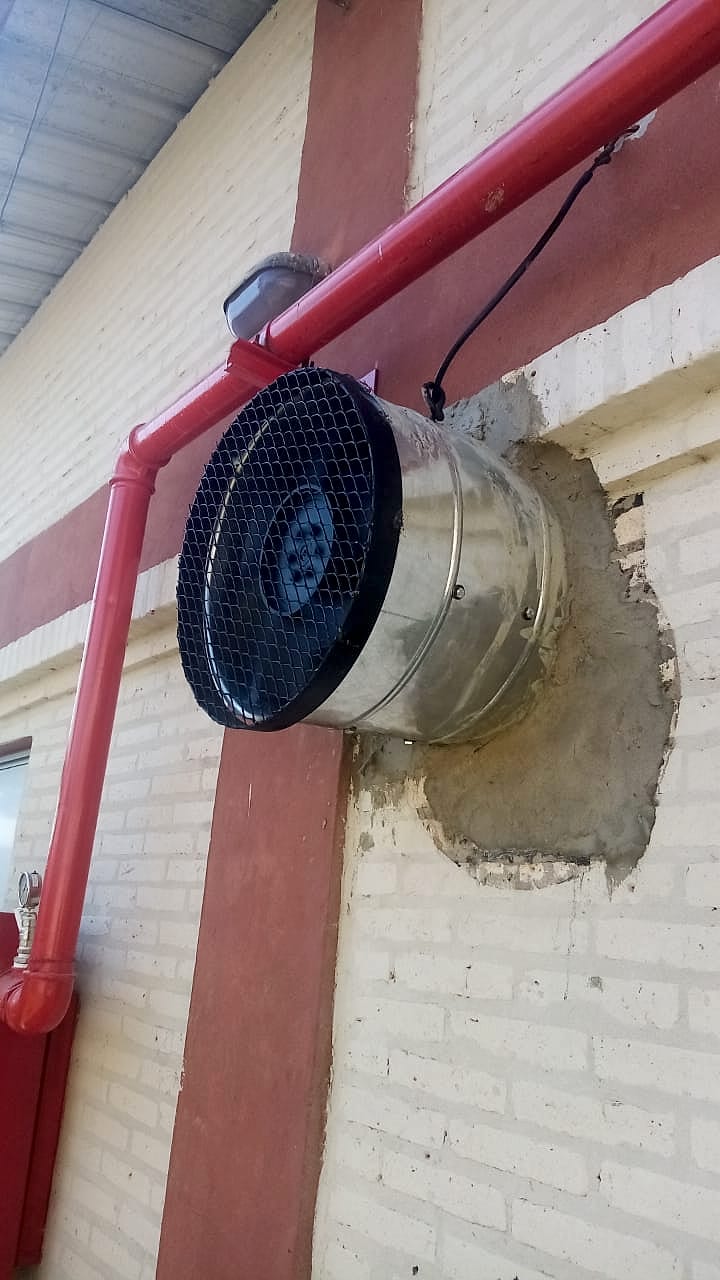 Extractor con rejilla protectora instalado en una pared de ladrillo, junto a una cañería roja