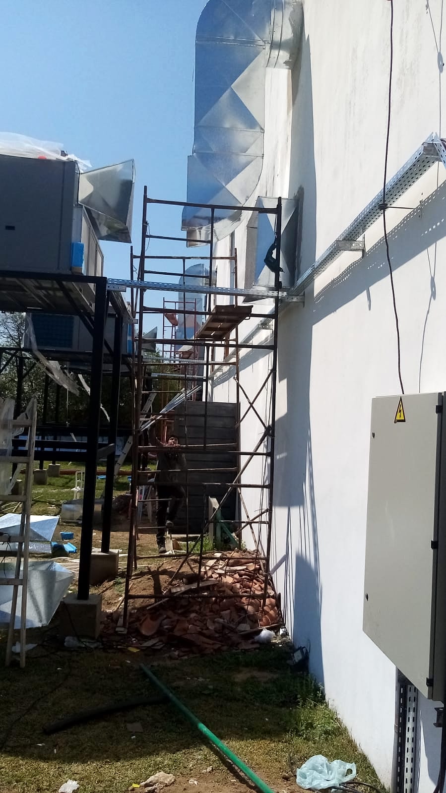 Ductos de chapa galvanizada tendidos por el exterior de un edificio con andamio; a la izquierda, equipos sobre una estructura metálica